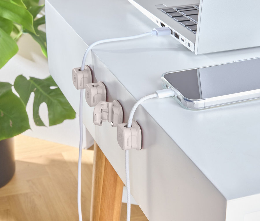 Stříbrný notebook a telefon se nabíjejí na bílém stole s dřevěnými držáky kabelů.