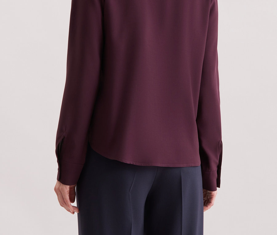 Zezadu je vidět žena s blond vlasy, která má na sobě purpurovou košili s dlouhým rukávem.