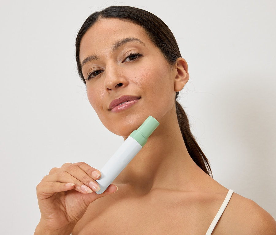 Žena drží bílo-zelenou láhev před obličejem.