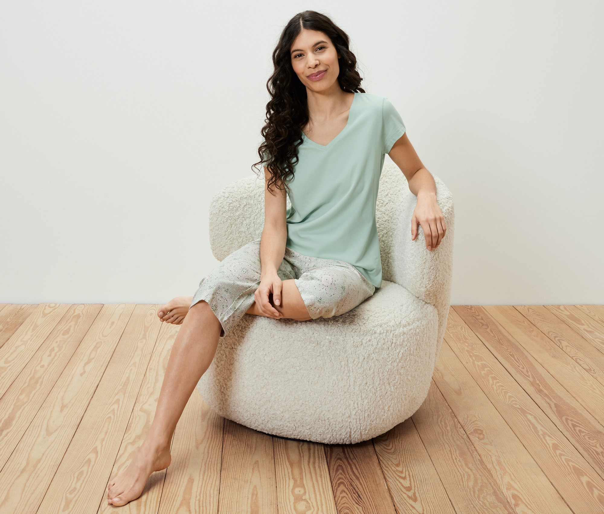 Žena sedí v křesle a má na sobě světle zelenou 3/4 pyžamovou soupravu.