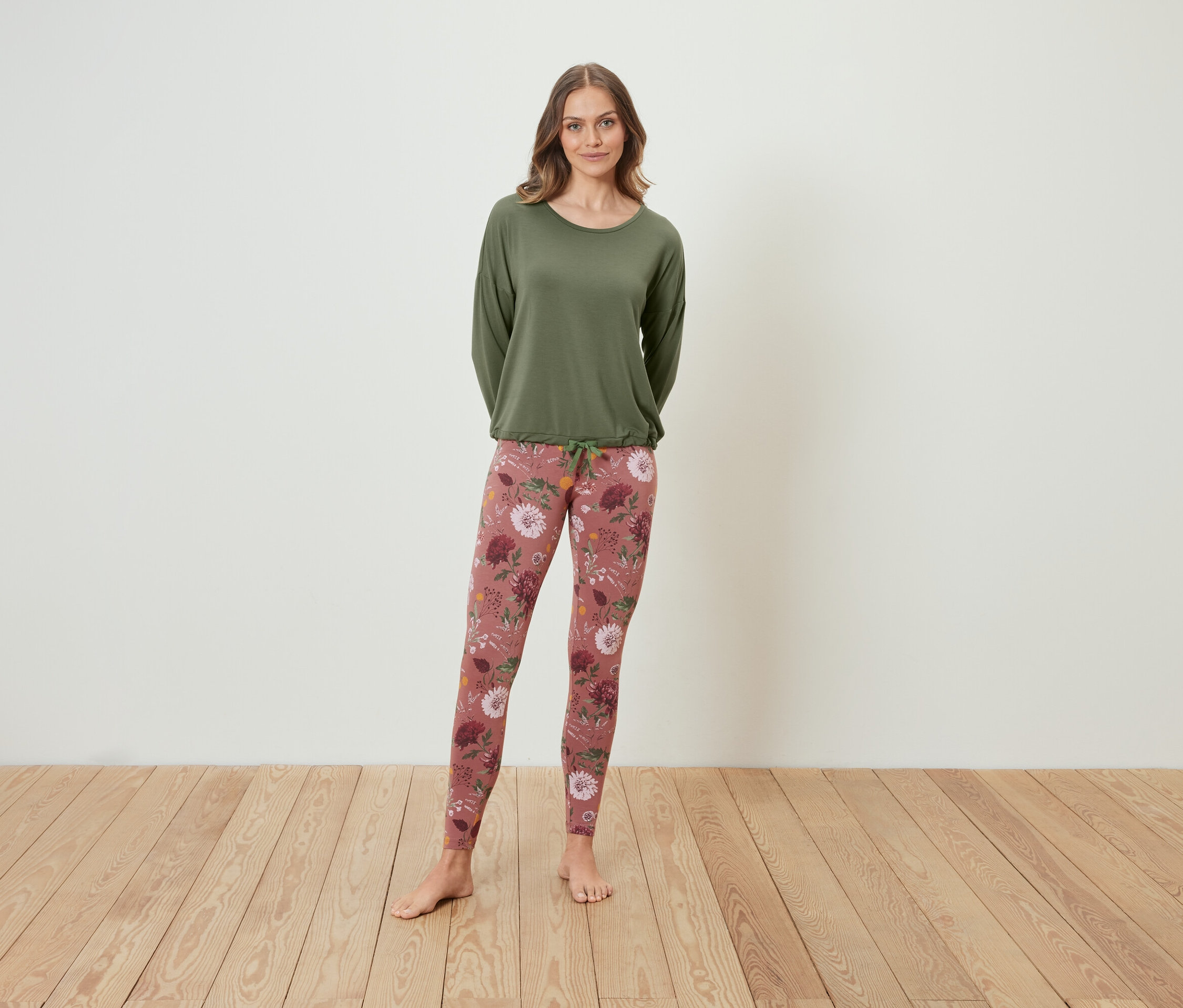 Žena stojí a má na sobě zelený top s dlouhým rukávem a květinové legíny.