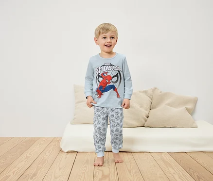 Chlapec v pyžamu s motivem Spidermana stojí na dřevěné podlaze před bílou pohovkou.