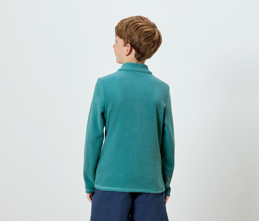 Zezadu je vidět osoba s krátkými hnědými vlasy, která má na sobě zelenomodrý top s dlouhým rukávem a námořnicky modré šortky.