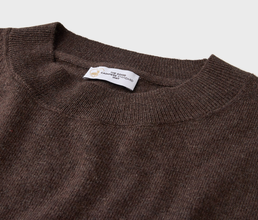 Detail hnědého svetru s kulatým výstřihem a štítkem.