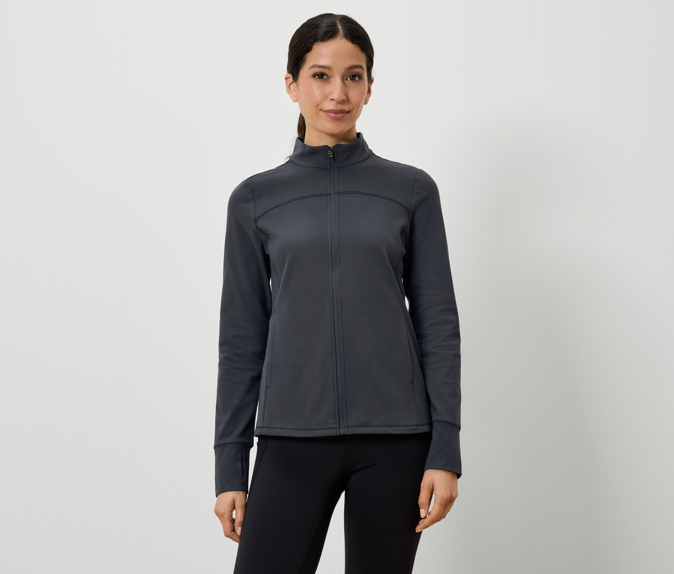 Žena má na sobě tmavě šedou sportovní bundu a černé legíny.