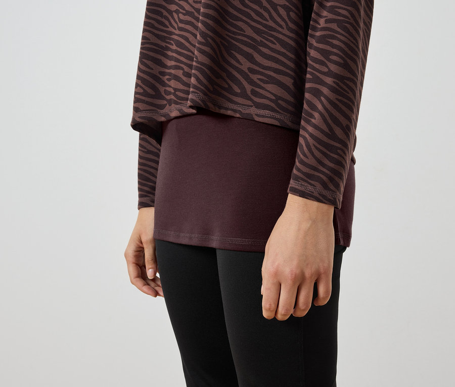 Detail ženy nosící hnědo-černou zebrovanou tuniku, vínový top a černé legíny.