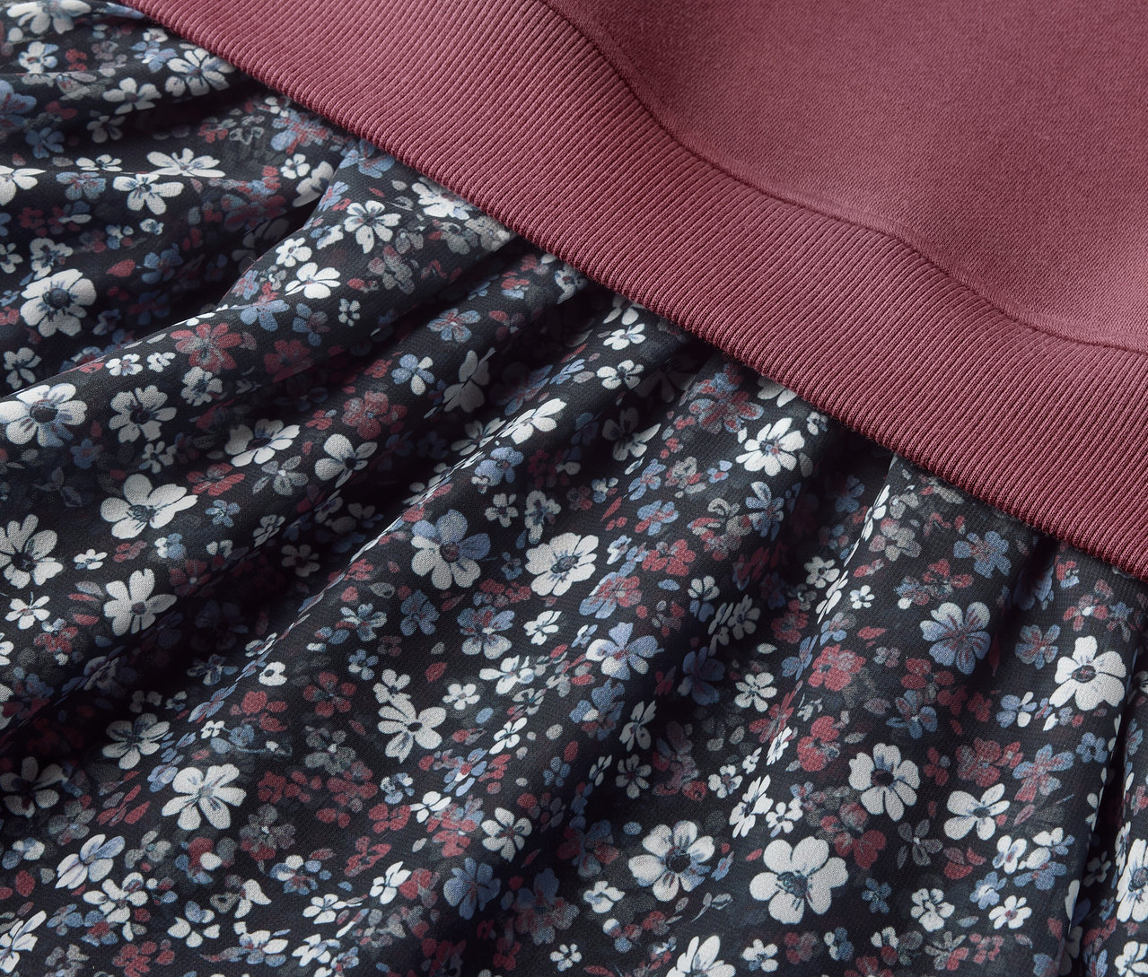 Detail dívčích teplákových šatů s květinovým vzorem na sukni a bordó vrškem.