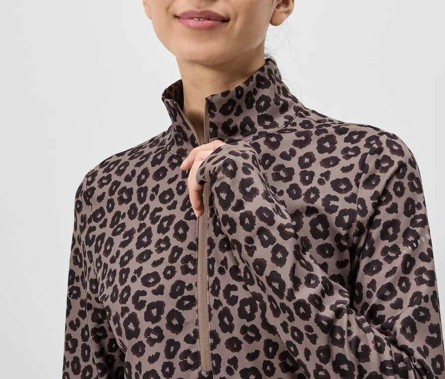 Žena v hnědém topu s dlouhým rukávem s leopardím vzorem, která si rozepíná zip.