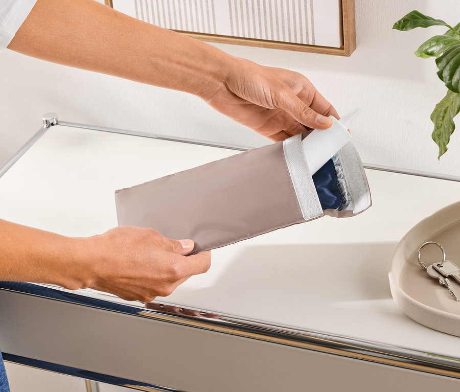 Osoba otevírá podlouhlý béžový ochranný obal, který obsahuje modrý produkt.