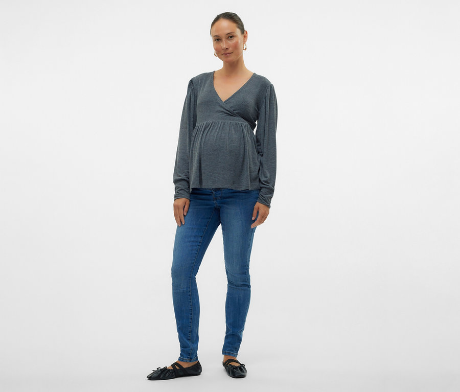 Žena v šedé zavinovací halence a skinny džínách MAMALICIOUS »MLMILA« pózuje na bílém pozadí.
