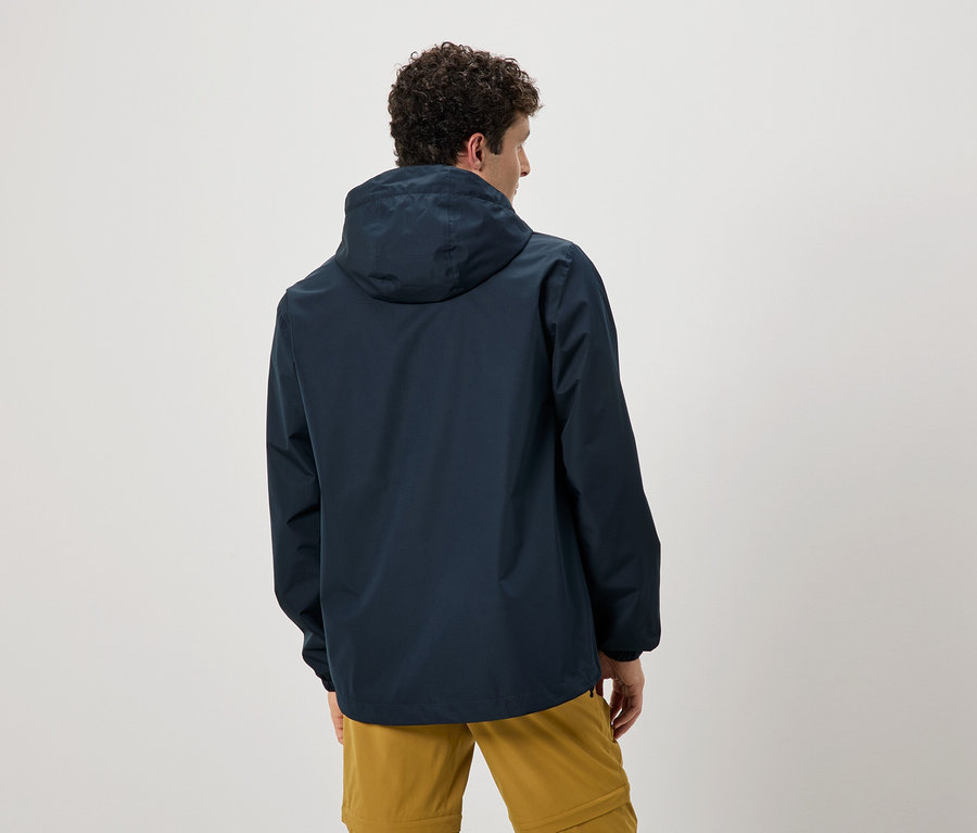 Pohled zezadu na muže s kudrnatými vlasy v tmavě modré bundě s kapucí a okrových kalhotách.