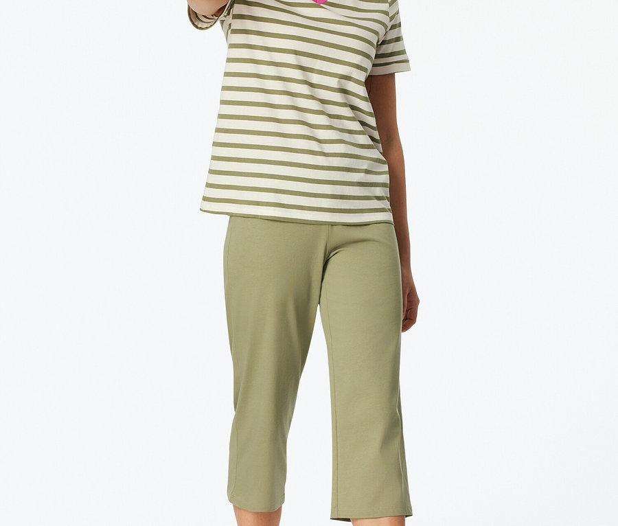 Žena stojí bosá a má na sobě pruhované tričko s výstřihem do V a zelené capri kalhoty.