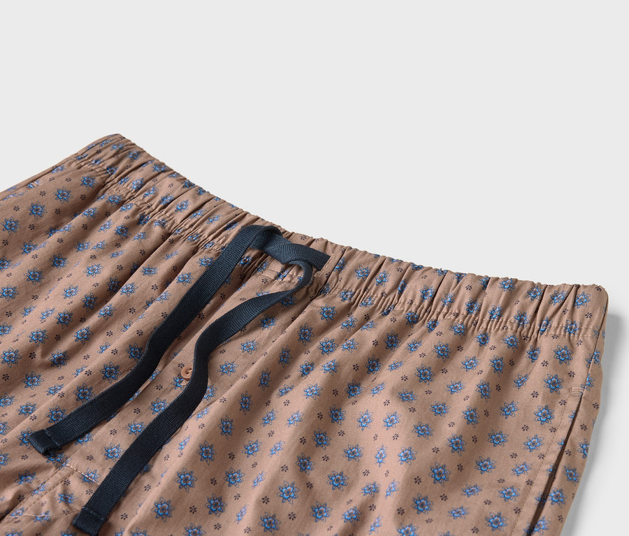 Detail béžových kalhot s modrým květinovým vzorem a tmavě modrou stahovací šňůrkou.