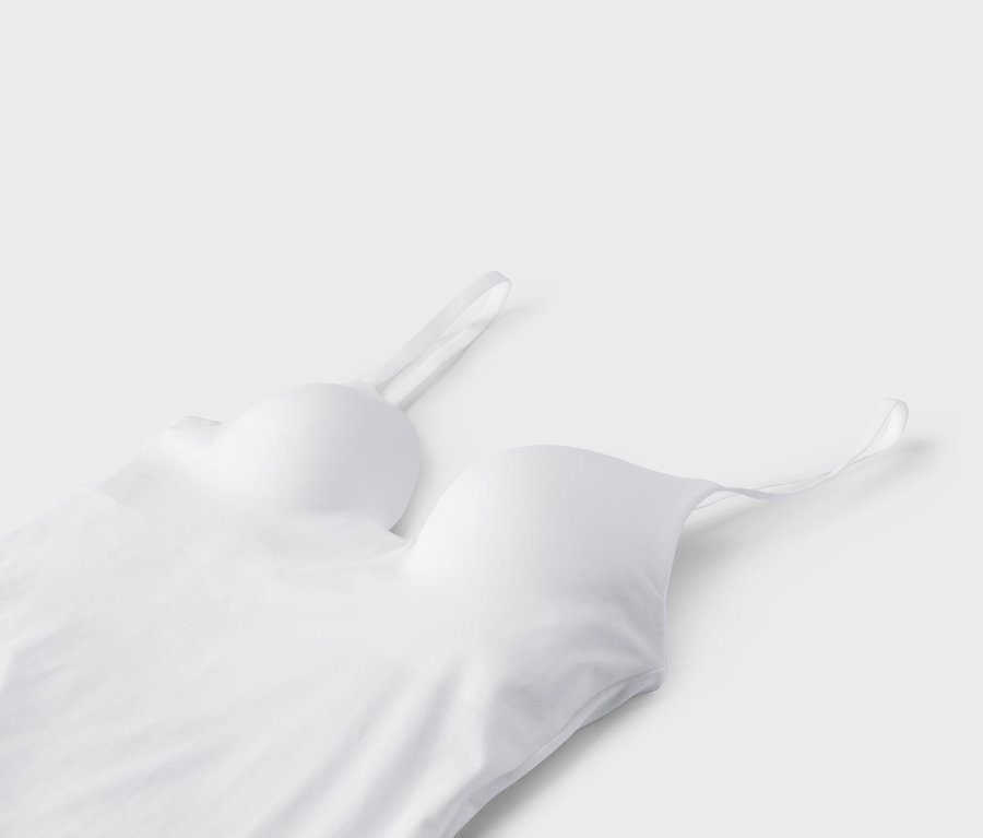 Detailní pohled na bílý bralette s tenkými ramínky na bílém pozadí.
