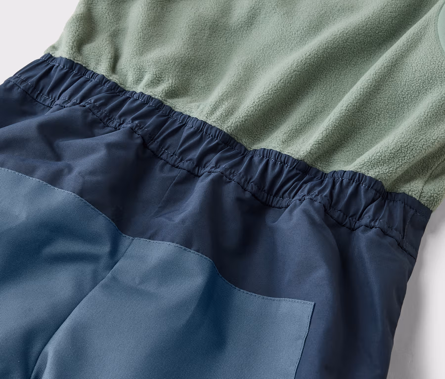 Detailní záběr kombinézy bez rukávů v zelené, námořnické a modré barvě s elastickým pasem.