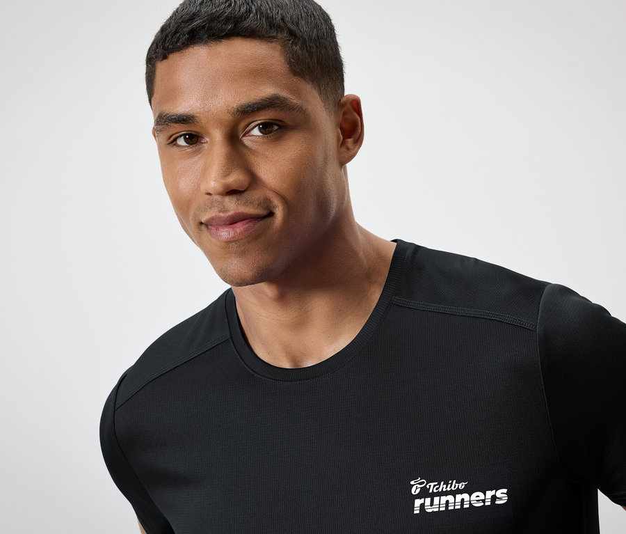 Muž s tmavou pletí má na sobě černé tričko s nápisem "Tchibo runners".