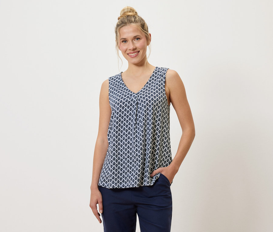 Žena s drdolem má na sobě modrobílý vzorovaný top a modré kalhoty, jednu ruku v kapse.