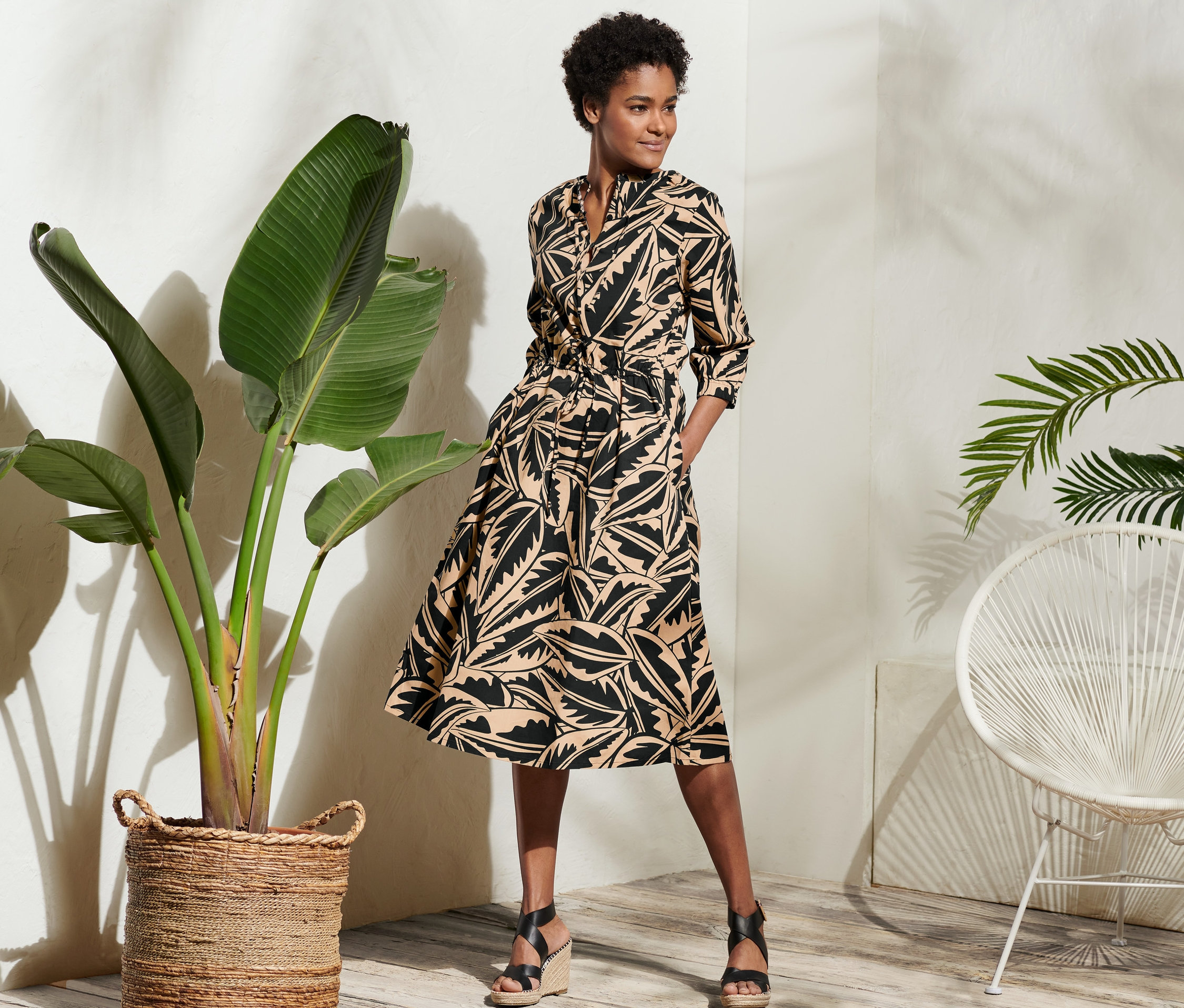 Žena pózuje v popelínových šatech s potiskem palmových listů.