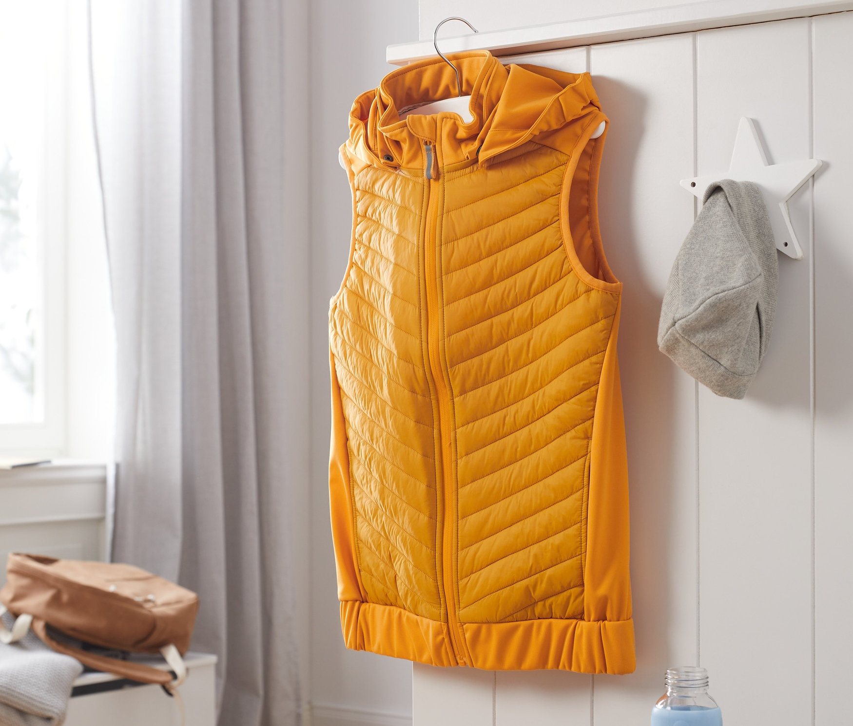 Žlutá hybridní softshellová vesta z recyklovaného materiálu visí na věšáku.