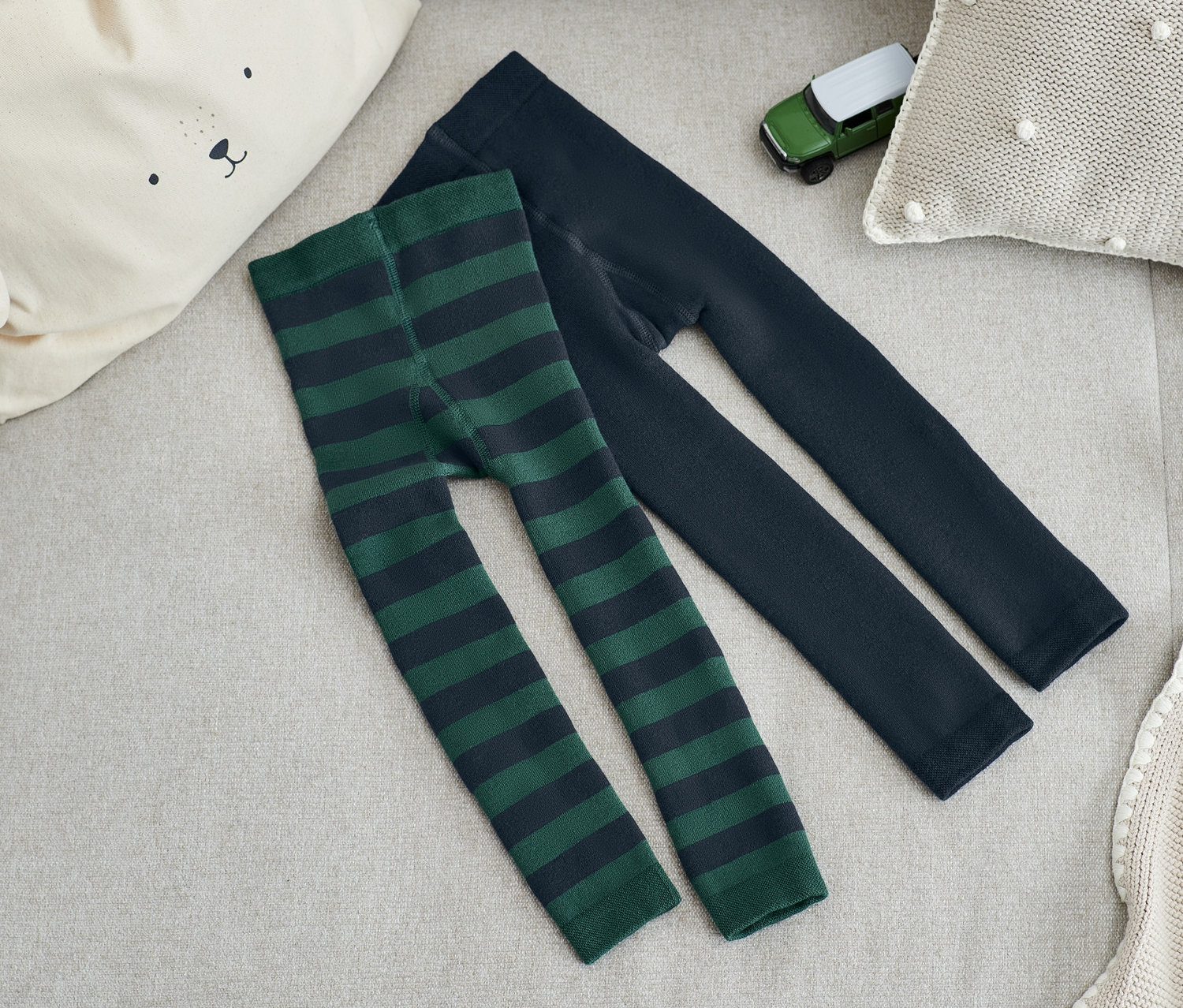 Dvoje termolegín na béžové pohovce, jedny zelené a pruhované, druhé tmavě modré.