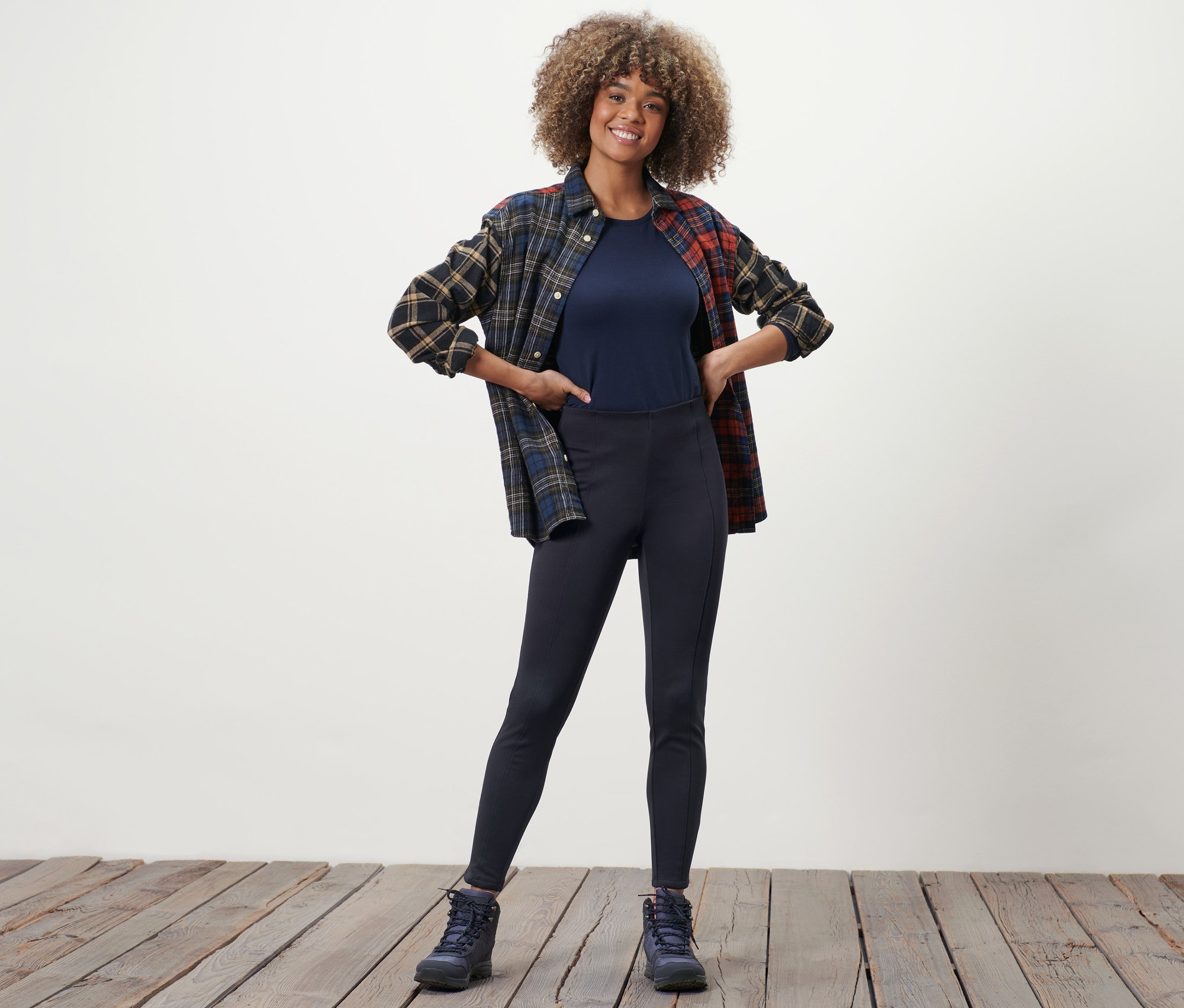 Žena pózuje v termolegínách, tričku a kostkované košili.