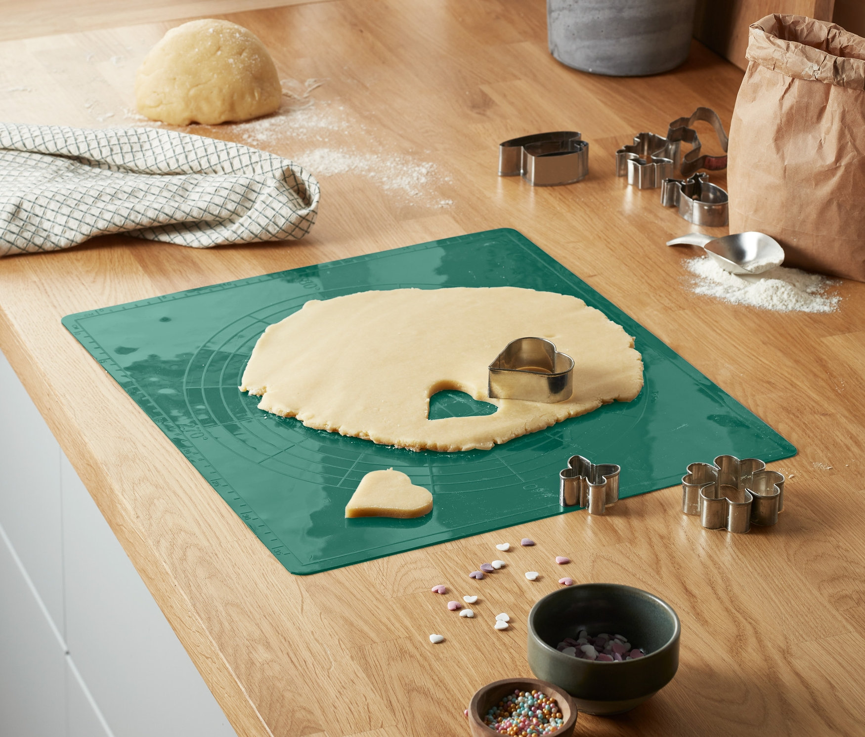 Na kuchyňské lince je zelená podložka na pečení k opakovanému použití s rozváleným těstem a vykrajovátky na sušenky.