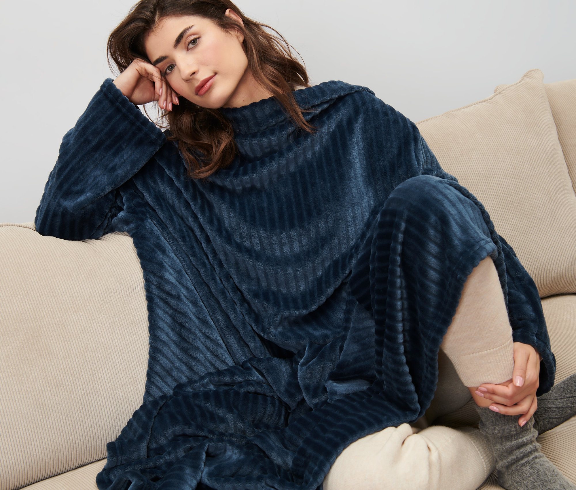 Žena sedí na gauči a má na sobě měkoučkou deku s rukávy.