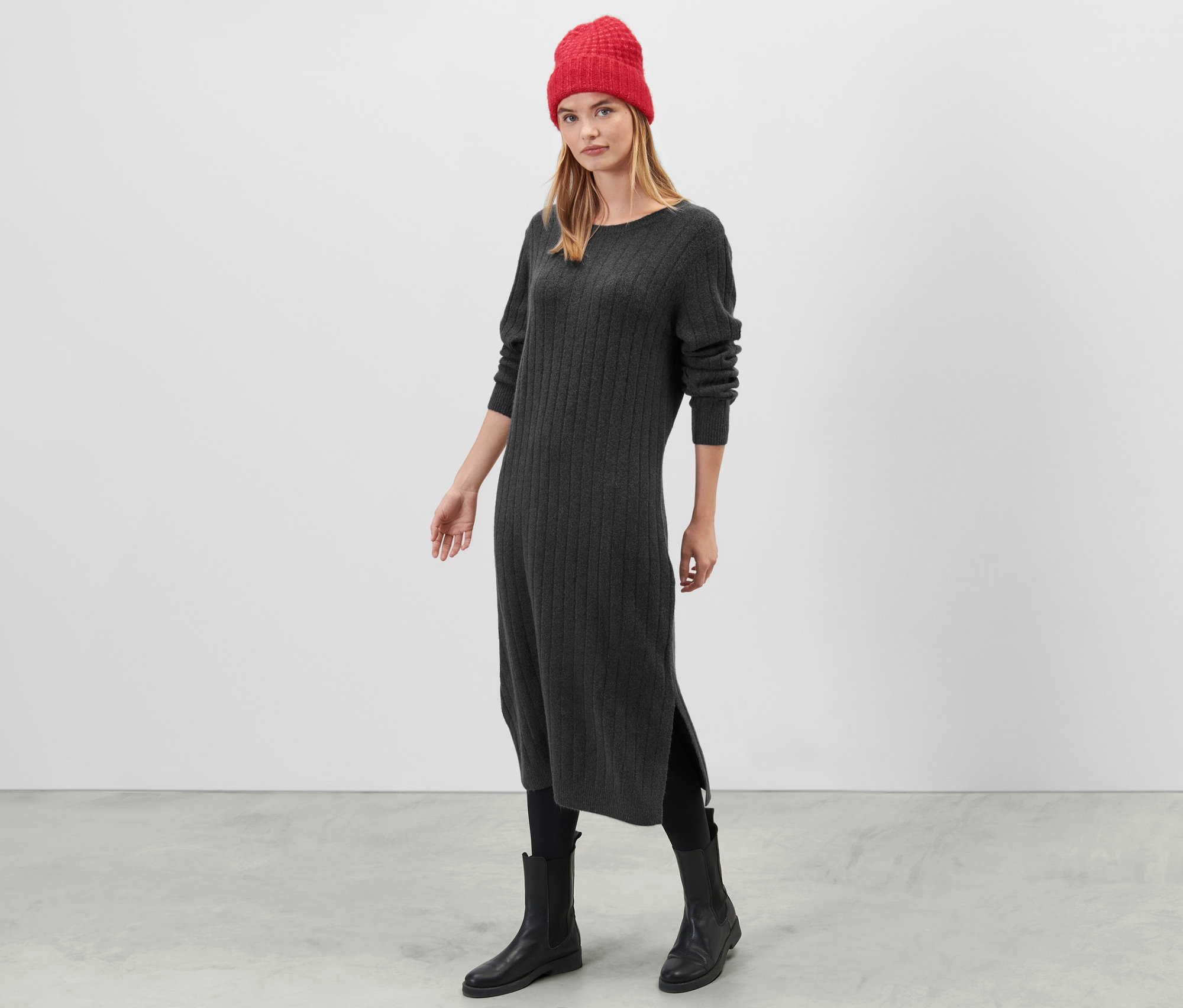 Žena stojí a má na sobě šedé žebrované pletené šaty.