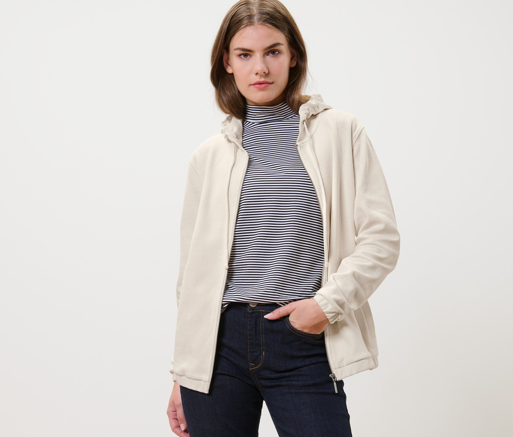 Žena má na sobě krémově bílou mikinu a džíny.