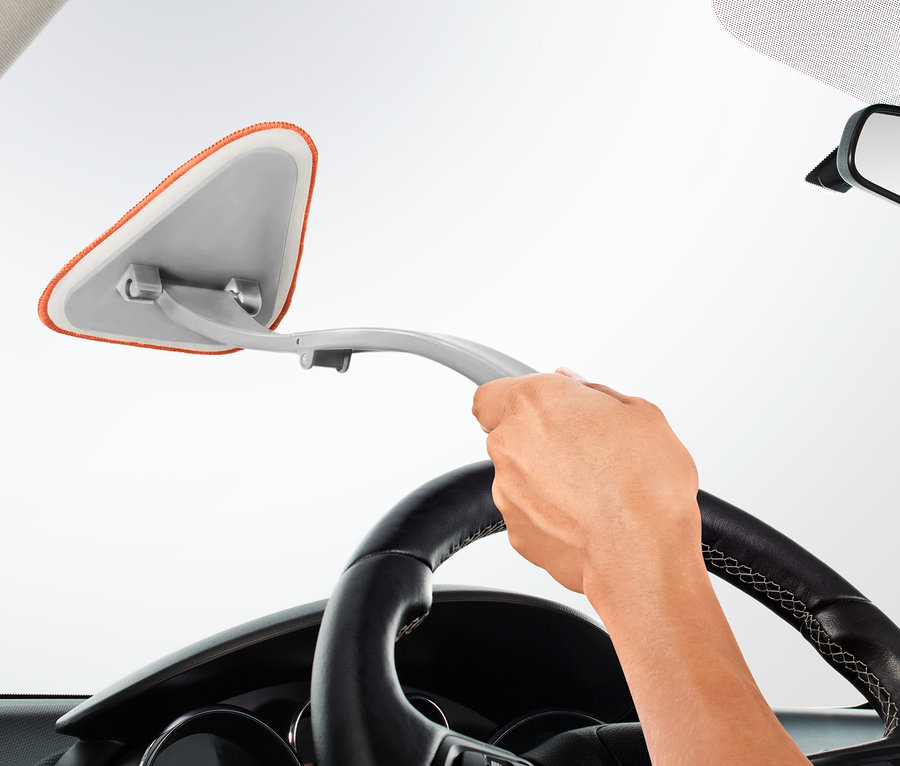 Ruka drží čistič autoskel a čistí čelní sklo auta.