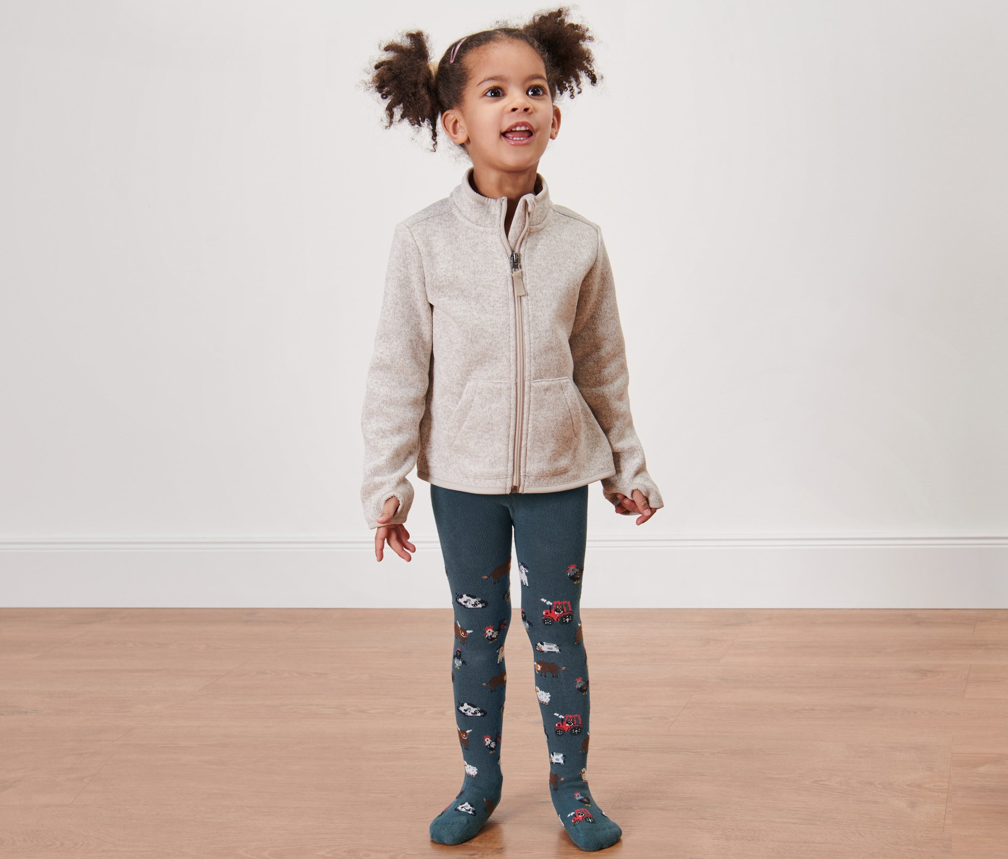 Holčička má na sobě 2 ks zelených punčocháčů s farmářským motivem.