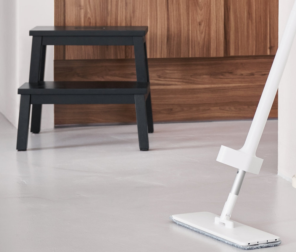 Na podlaze stojí mop s funkcí postřikování, vedle něj je skládací úklidový kbelík. V pozadí jsou schůdky se 2 schody.