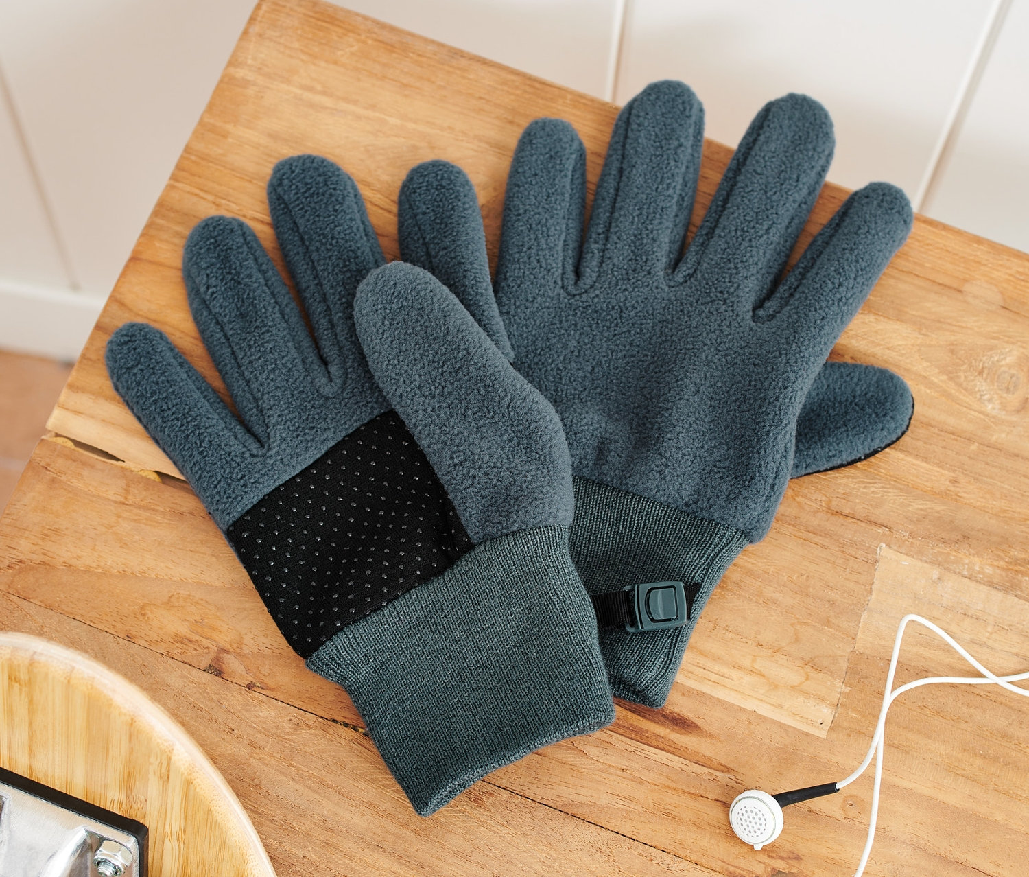 Dvoje dětské fleecové rukavice leží na dřevěné lavici vedle skateboardu a sluchátek.