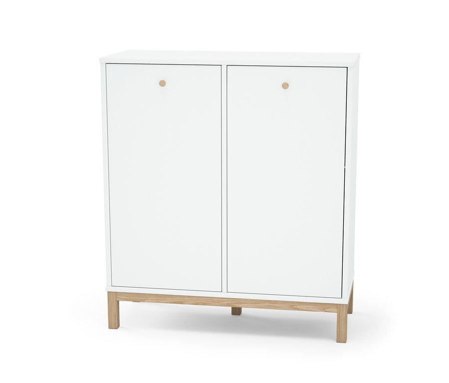 Bílý regál s košem na prádlo má dvoje dveře s kulatými úchyty a stojí na dřevěných nohách.