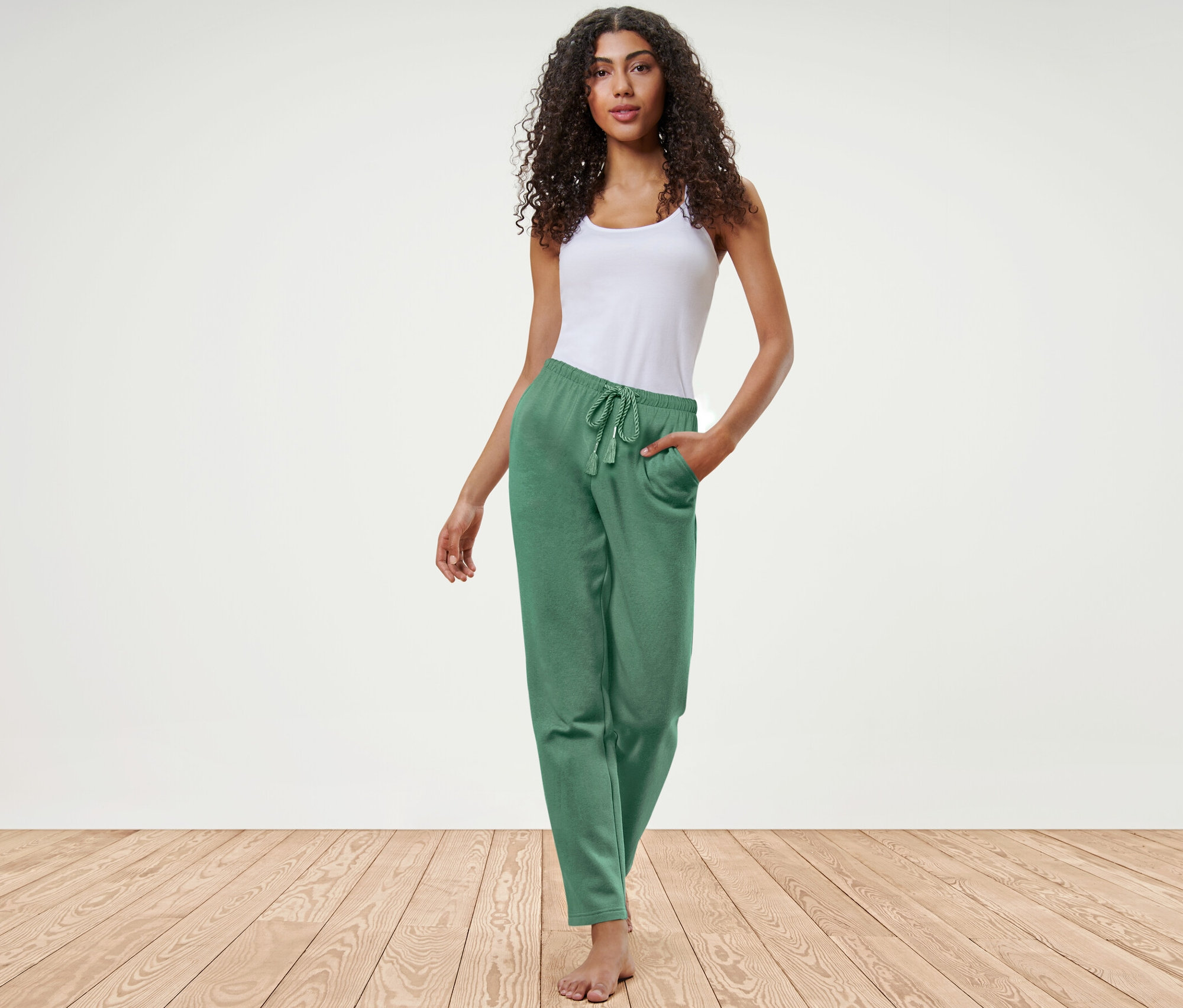 Žena pózuje v zelených pohodlných kalhotách a bílém topu.