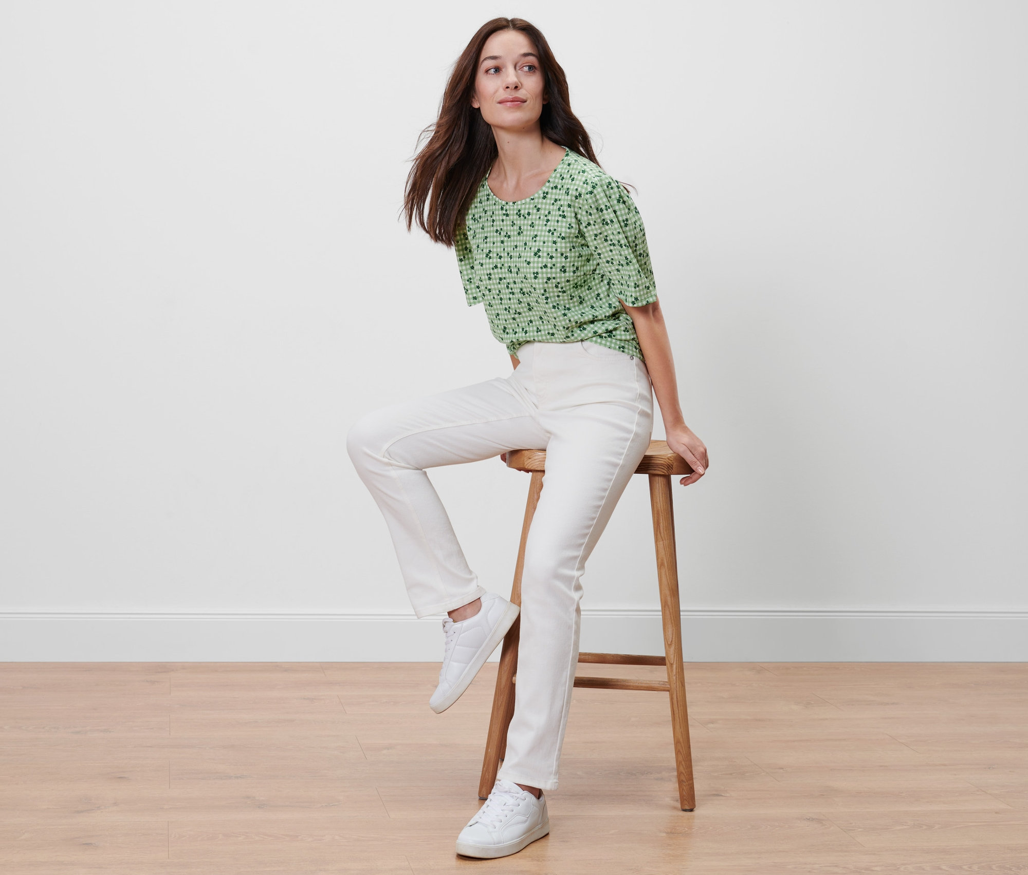 Žena sedí na stoličce a má na sobě zelené halenkové triko s celopotiskem.