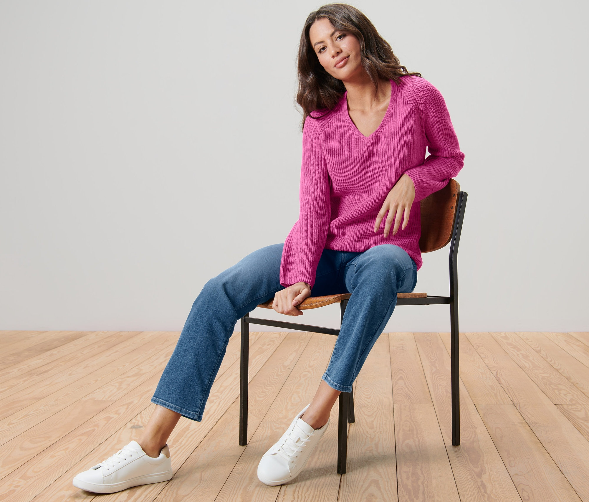 Žena sedí na židli a má na sobě růžový pletený svetr.