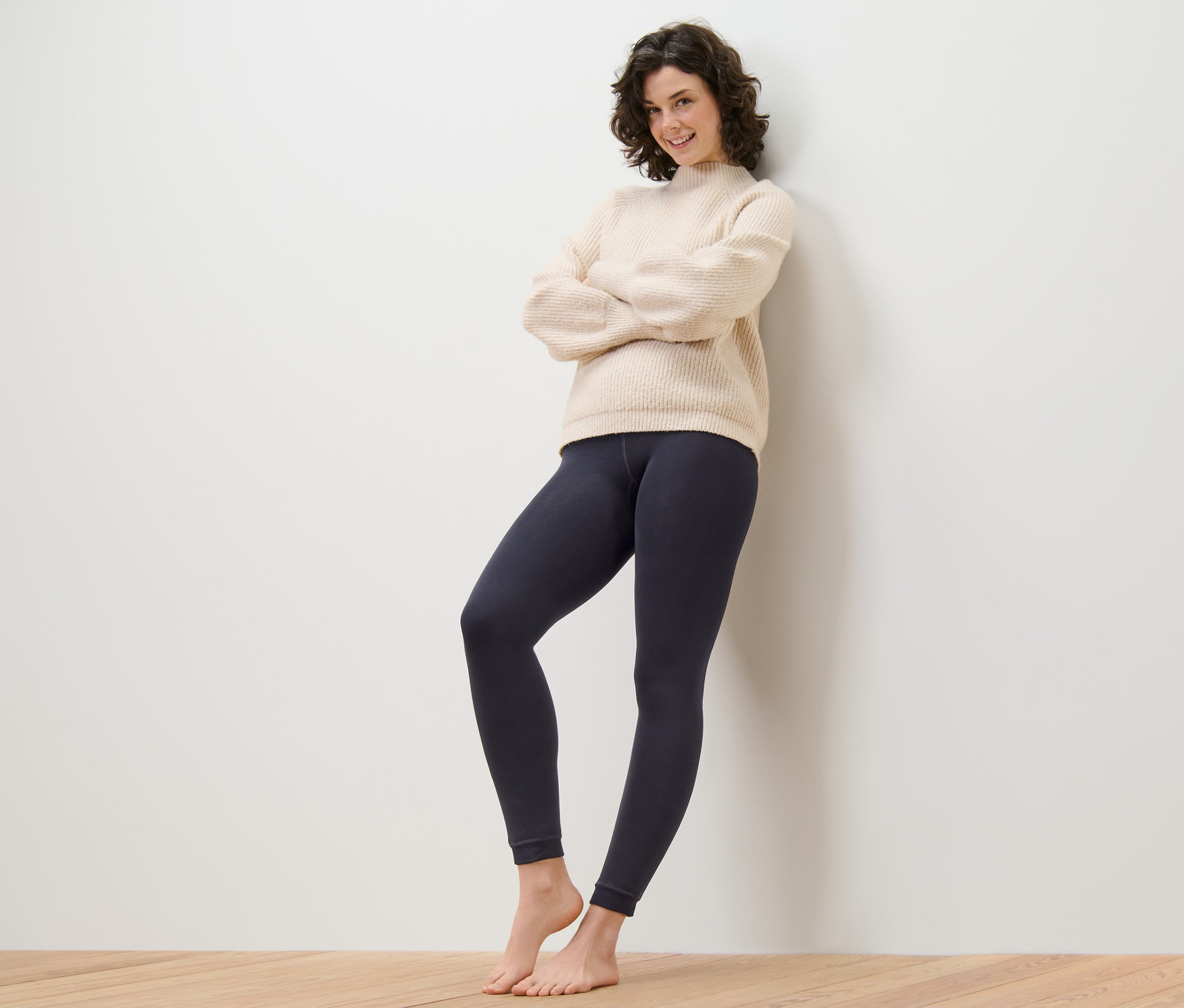 Žena se zkříženýma rukama stojí opřená o zeď a má na sobě podšité legíny.