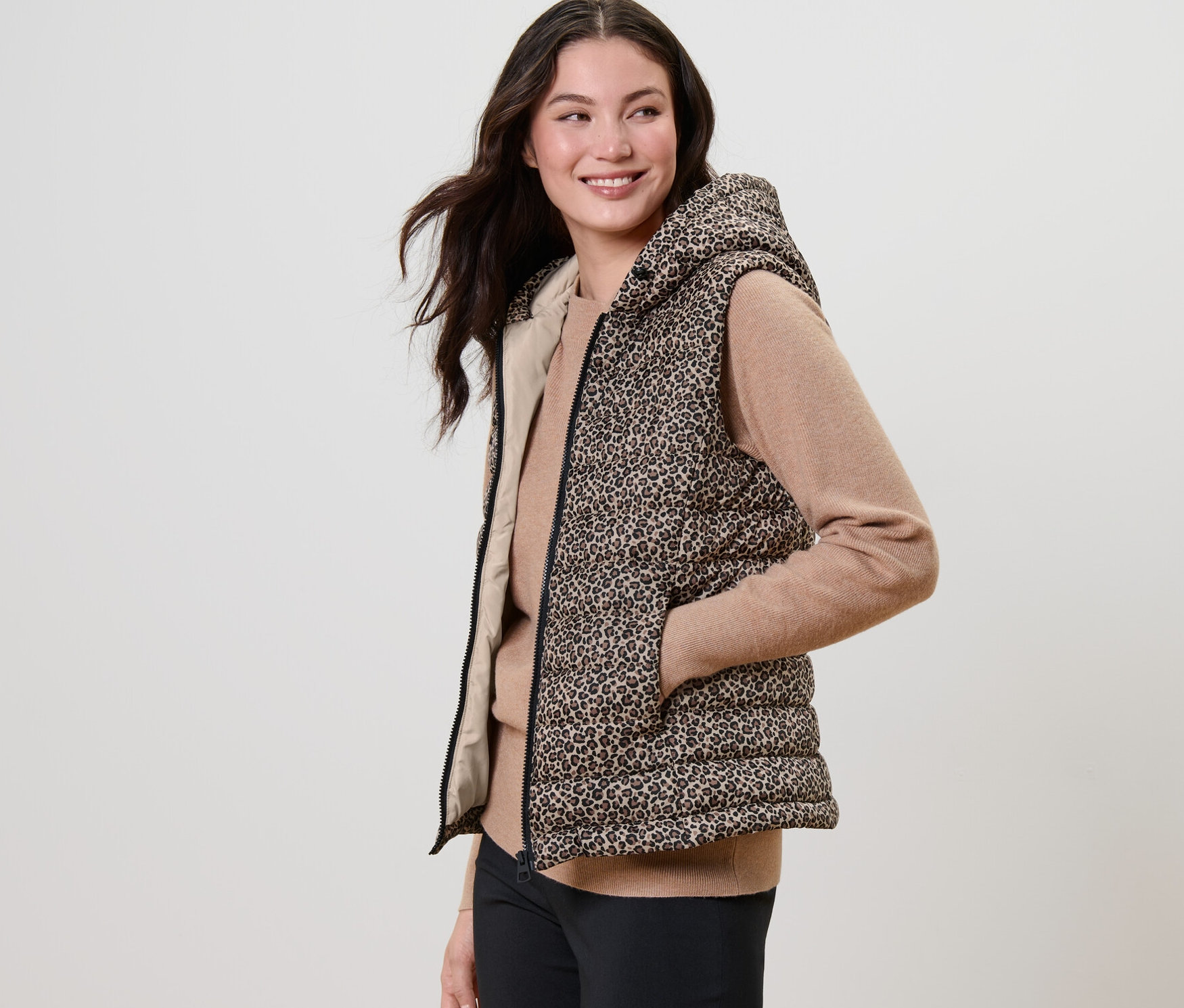 Žena pózuje v prošívané vestě s kapucí a potiskem.