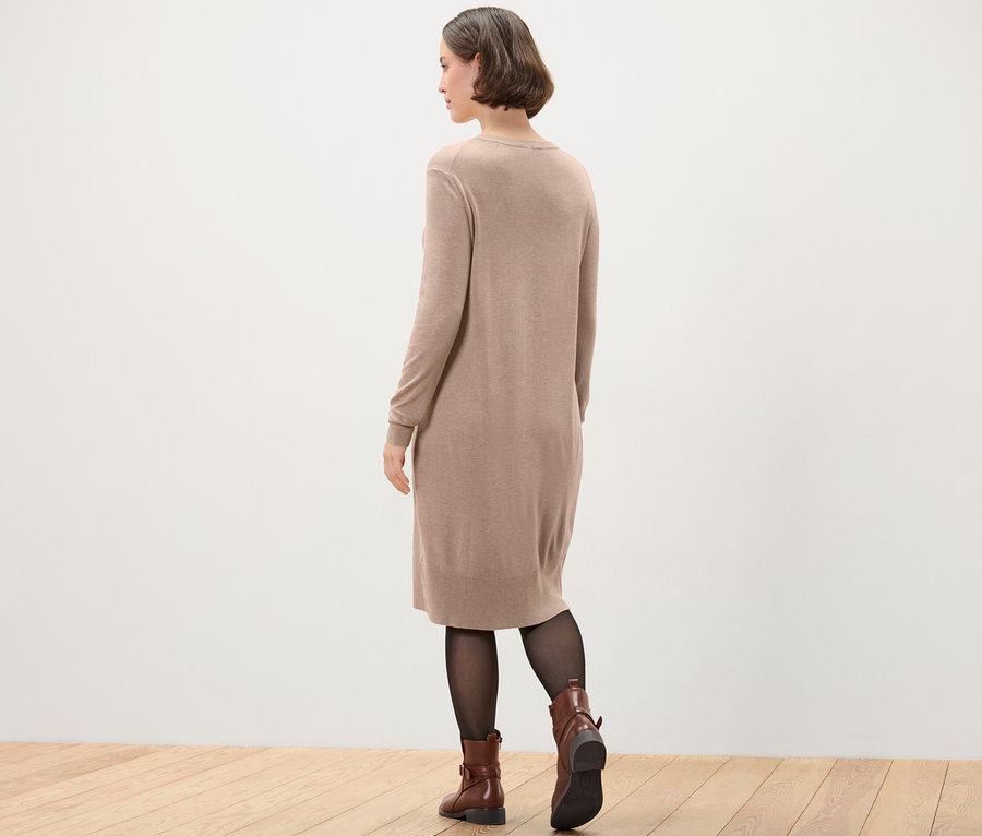 Žena v hnědých šatech z jemného úpletu, černých punčochách a hnědých botách.