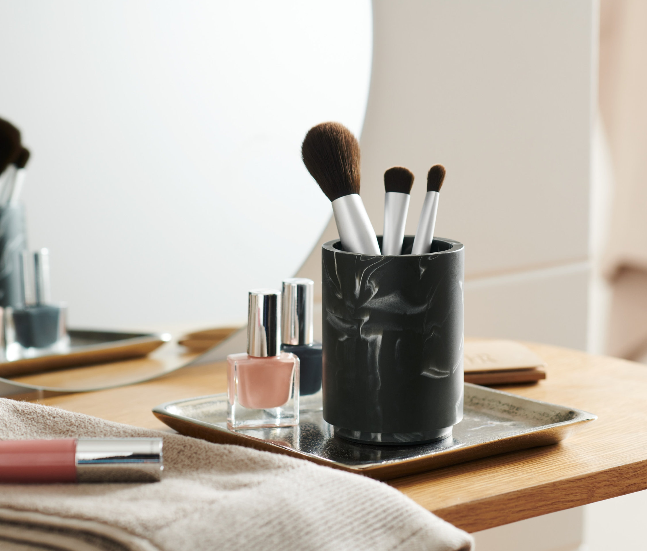 Štětce na make-up v mramorovém kelímku vedle laků na nehty na podnosu.