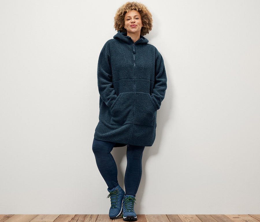 Žena pózuje ve sportovních legínách a plyšovém kabátu oversized.