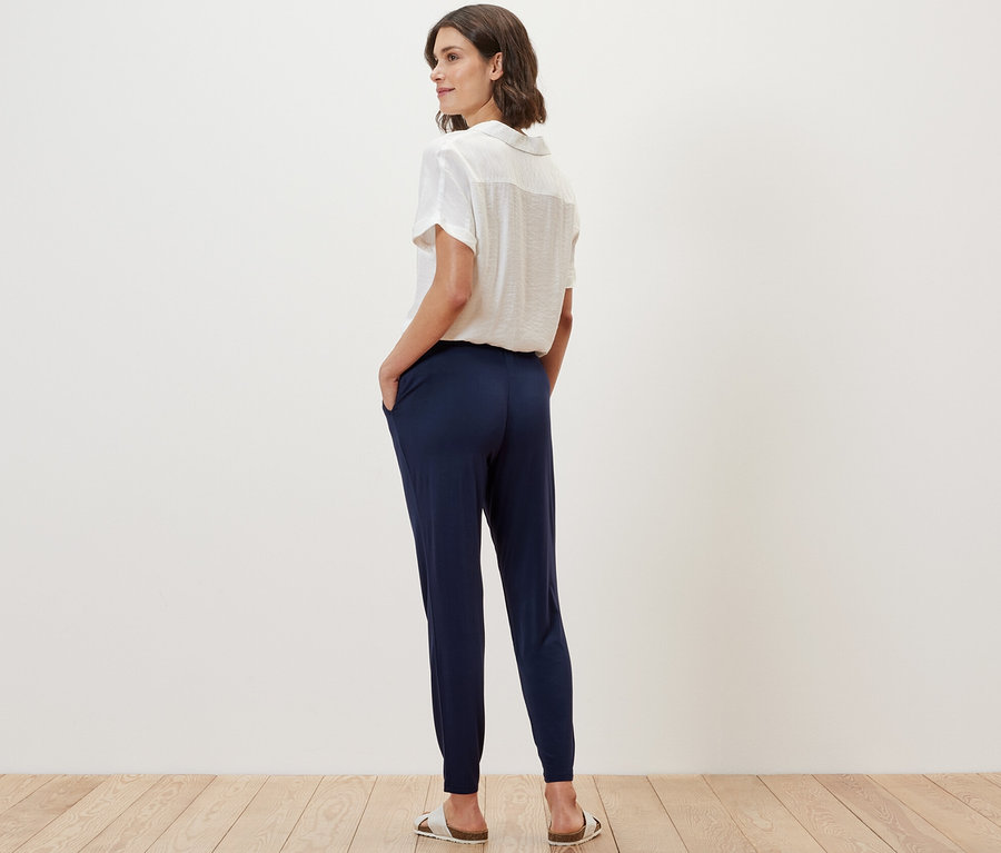 Žena stojí zády k fotoaparátu a má na sobě tmavě modré žerzejové kalhoty.