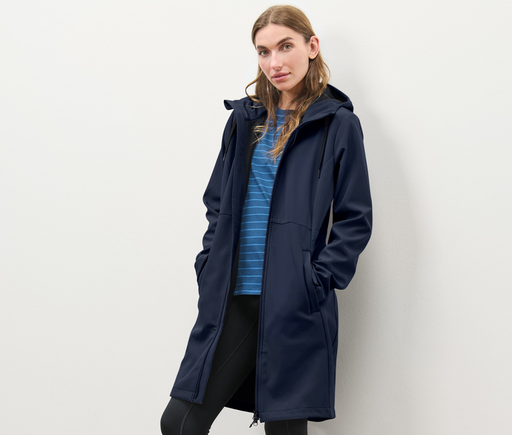Žena pózuje v modrém softshellovém kabátě.