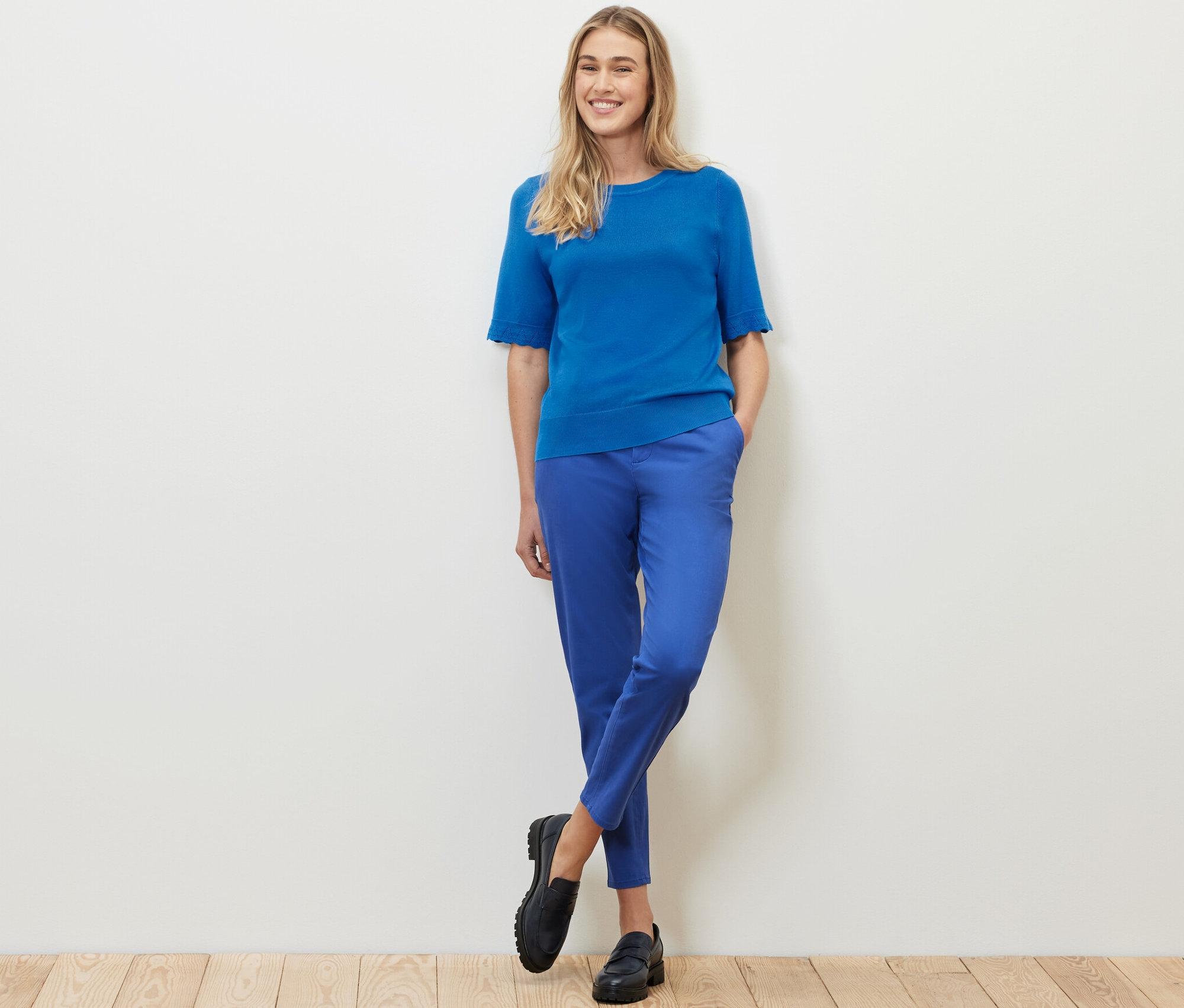 Žena stojí a pózuje v kobaltově modrém svetru z jemného úpletu a modrých kalhotách.