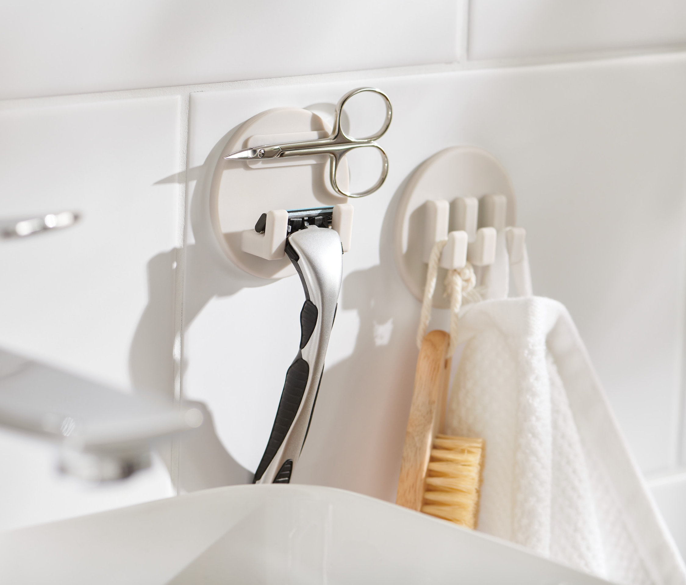 Dva samolepicí držáky na bílých kachličkách, v jednom je umístěna žiletka a nůžky.