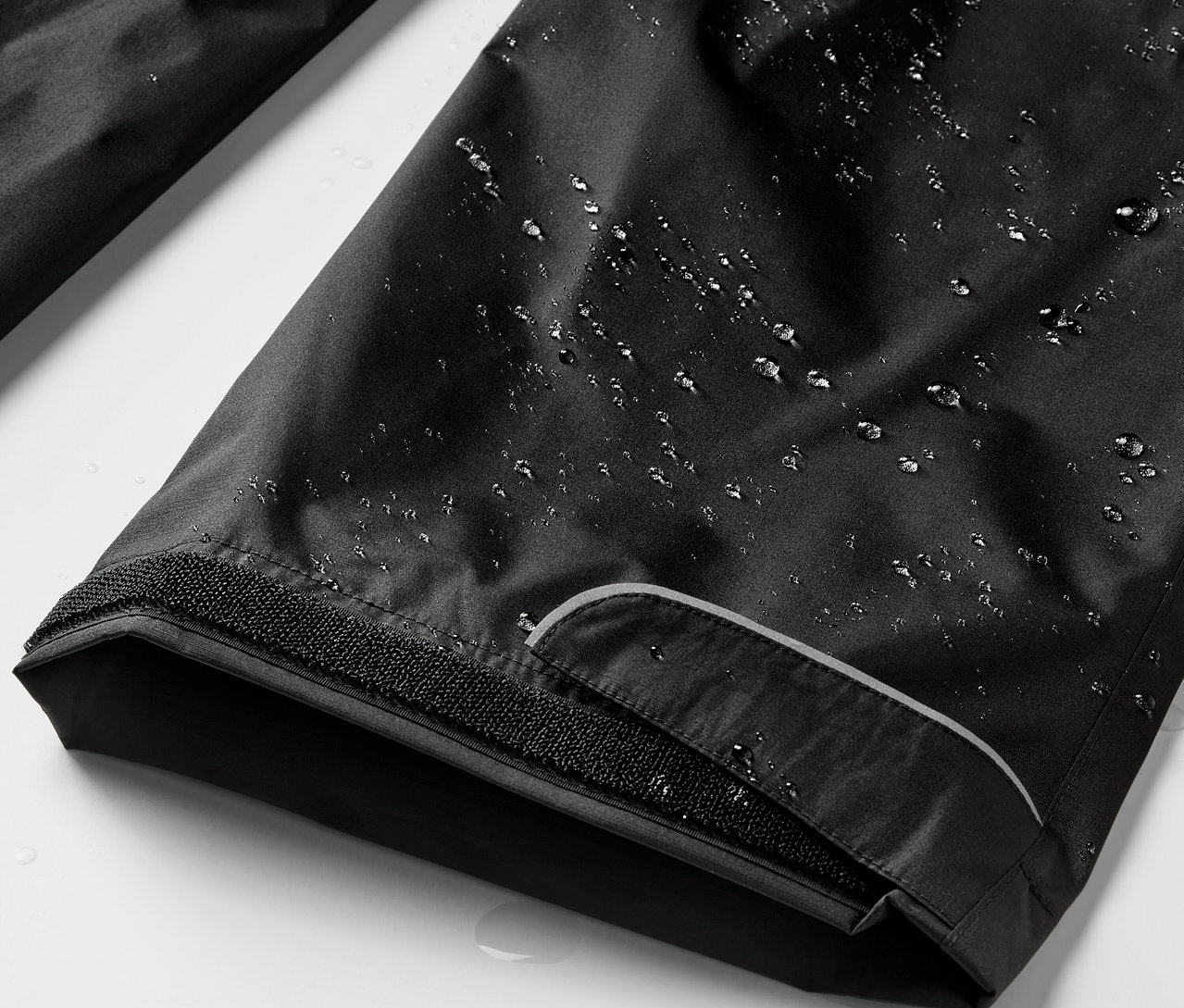 Detailní záběr na černé kalhoty do deště s kapkami vody.