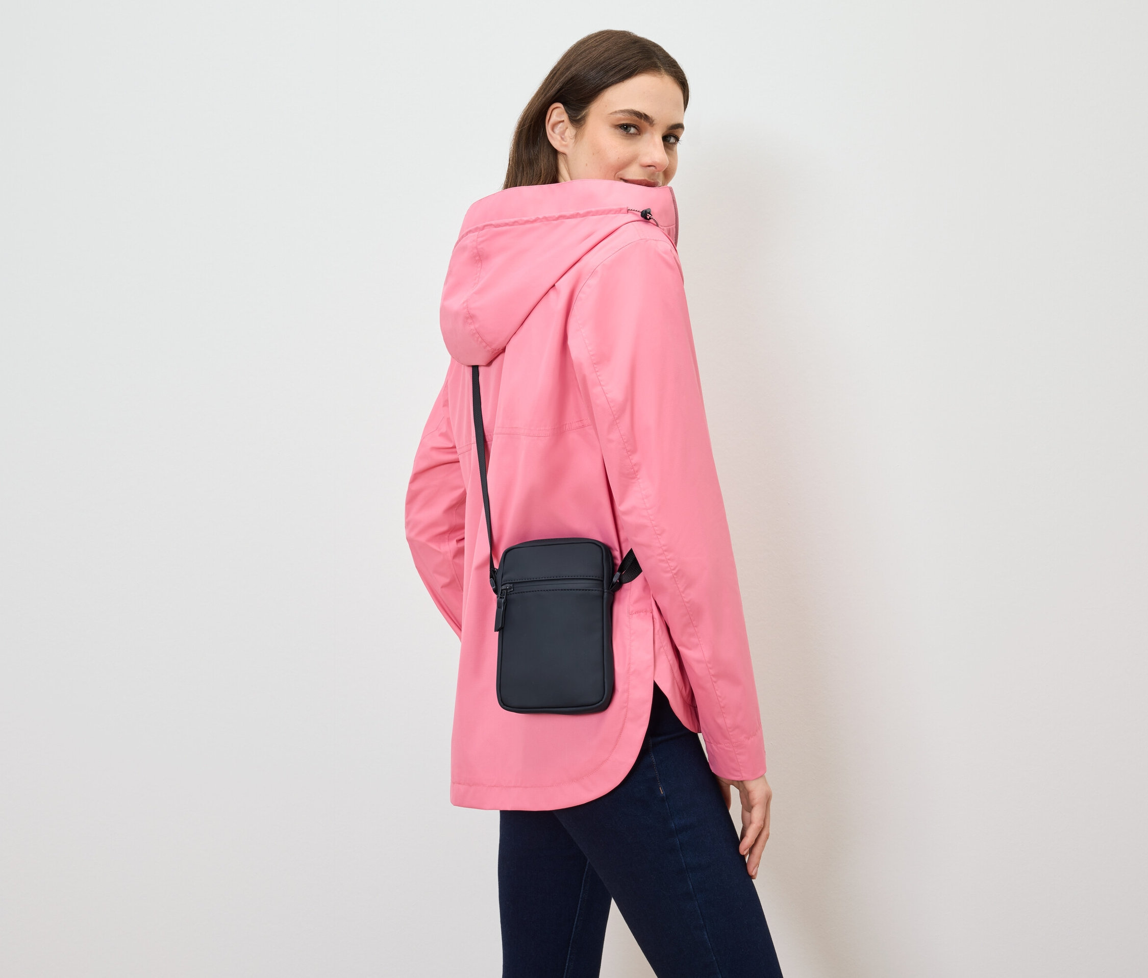 Žena se dívá přes rameno, má na sobě růžovou bundu a černou tašku přes rameno.