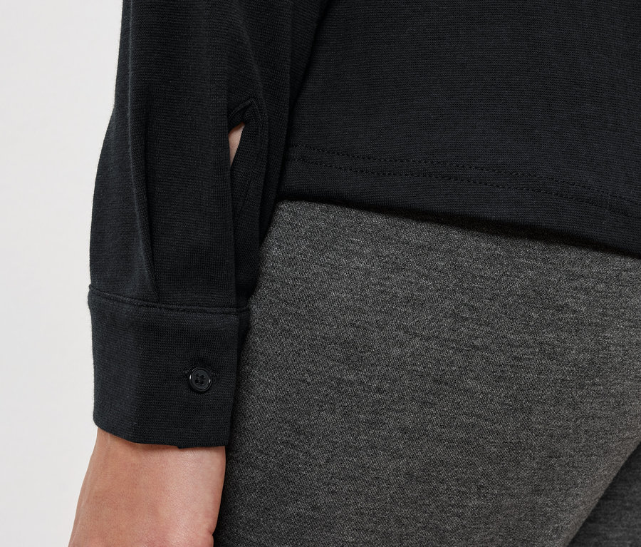 Detail dámského outfitu s černou blůzou a šedými legínami.