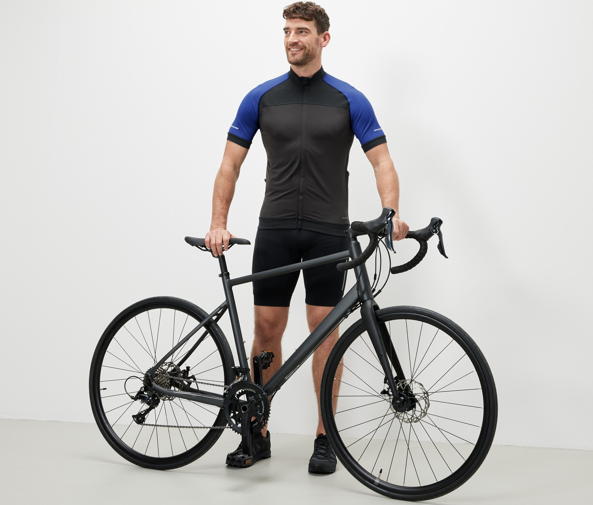 Muž stojí vedle kola v modrém cyklistickém trikotu.